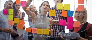 people placing sticky notes on a clear board